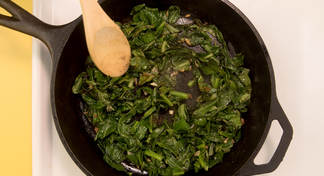 wooden spoon stirring greens in cast iron skillet on stove