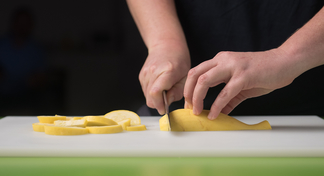 Hands chopping yellow squash on chopping board