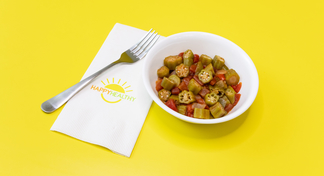 A white bowl of Tomatoes and Okra on a yellow background next to a HappyHealthy napkin and fork