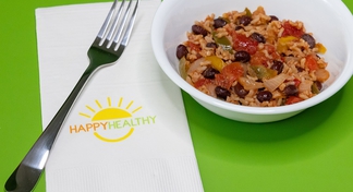 A white bowl of Black Beans and Rice on a green background next to a fork and napkin