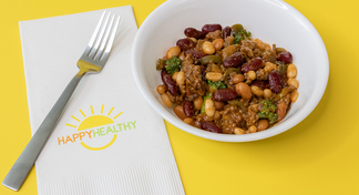 A white bowl with Beef, Bean and Broccoli Skillet next to a fork and HappyHealthy napkin on a yellow background