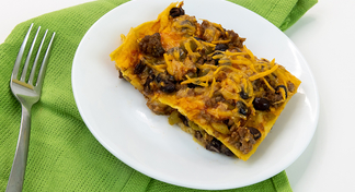 A slice of beef enchilada casserole on a white plate laying on a green towel