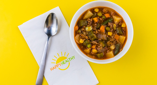 Beef Vegetable Soup in a bowl next to a spoon and Happy Healthy napkin