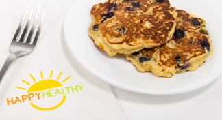 A white plate of blueberry oatmeal pancake next to a fork and HappyHealthy napkin