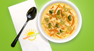 A bowl of broccoli and cheese soup next to a spoon and HappyHealthy Napkin