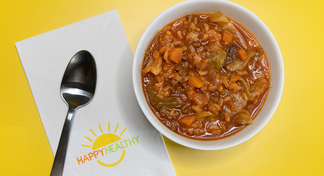 A bowl of cabbage roll soup next to a spoon and HappyHealthy napkin