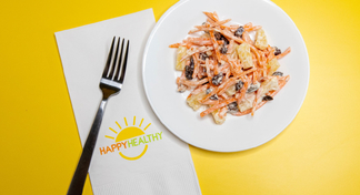 A white plate with carrot salad next to a Happy Healthy napkin and fork