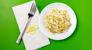 Coleslaw on a white plate with HappyHealthy napkin and fork to the left side.