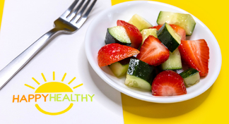 A white plate with cucumber strawberry salad next to a fork and HappyHealthy napkin