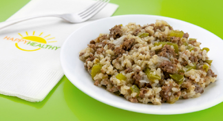 A white plate full of dirty rice on a green background next to a fork and HappyHealthy Napkin