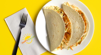 A white plate with two fish tacos next to a fork and Happy Healthy napkin