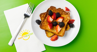French toast topped with blackberries and raspberries on a white plate next to a Happy Healthy Napkin and Fork