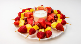platter with chunks of fresh fruit on toothpicks and container of vanilla yogurt