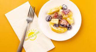 Creamy Fruit Salad on white plate next to HappyHealthy napkin and fork
