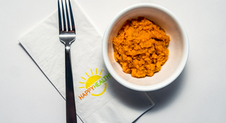 Bowl of mashed sweet potatoes with fork on HappyHealthy napkin.