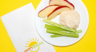 A dollop of peanut butter dip surrounded by celery and apple slices on a white plate next to a happy healthy napkin