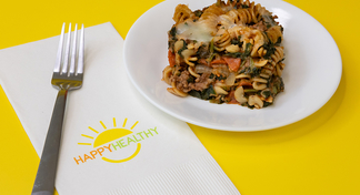 a plate of pizza casserole on a yellow background next to a HappyHealthy napkin and fork