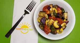A bowl of oven roasted ratatouille vegetables next to a fork and HappyHealthy Napkin