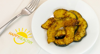 A white plate with roasted acorn squash next to a fork and HappyHealthy napkin
