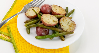 A white plate of Roasted Green Beans and Red Potatoes on a yellow cloth napkin
