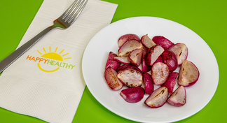 a plate of Roasted Radishes on a green background next to a HappyHealthy napkin and fork