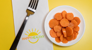A white bowl of sautéed carrots next to a fork and HappyHealthy napkin