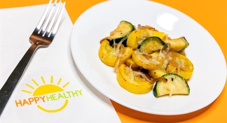 A white plate with sauteed squash next to a fork and HappyHealthy napkin