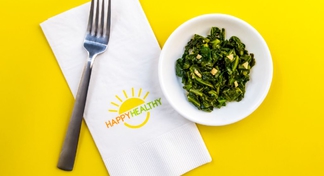 A plate of cooked greens, a fork, and a napkin stamped with the Happy Healthy logo.
