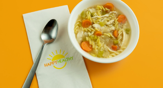 A bowl of slow cooker chicken noodle soup next to a HappyHealthy napkin and spoon