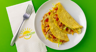 Two Slow Cooker Chicken Tacos on white plate next to HappyHealthy napkin with fork