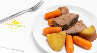 A white plate with carrots, potatoes, and pot roast next to a fork and happyhealthy napkin