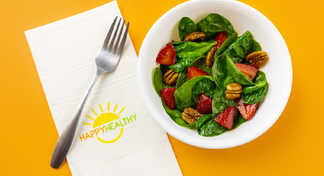 Strawberry Spinach Salad in a white bowl next to a HappyHealthy napkin and fork