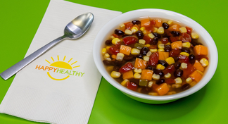 A bowl of Sweet Potato and Corn Soup on a green background next to a fork and HappyHealthy Napkin