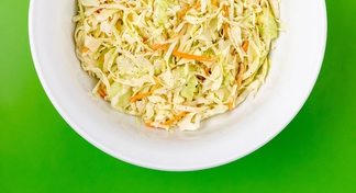 Coleslaw in a white bowl with green background color. 