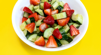 A white bowl filled with Cucumber Strawberry Salad on a yellow background