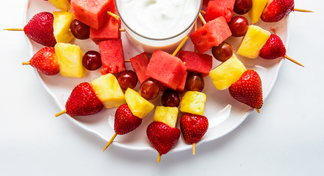 platter with chunks of fresh fruit on toothpicks and container of vanilla yogurt