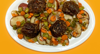 A white plate filled with beef patties, cooked potatoes, peppers and carrots