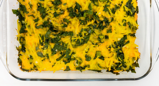 A baked dish of hash brown casserole topped with spinach and melted cheese
