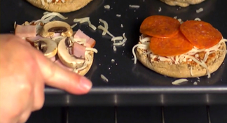 A hand sliding a tray with mini pizzas into an oven