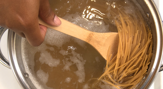 A person stirs a pot of boiling whole grain pasta.