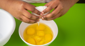 Eggs being cracked into a bowl filled with egg yolks and whites