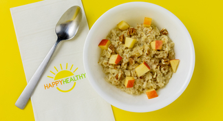  A bowl of oatmeal topped with apples and walnuts in a white bowl next to a spoon and HappyHealthy Napkin