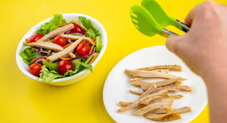 A plate of chicken strips, a bowl of salad and a hand with tongs over the chicken