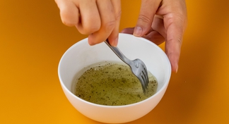 hand mixing italian dressing with a fork in a white bowl.