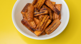 A white bowl filled with roasted carrots on a yellow background