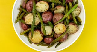 A white bowl of Roasted Green Beans and Red Potatoes on a yellow background
