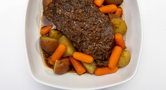 A white bowl with potatoes, carrots and pot roast smothered in onions