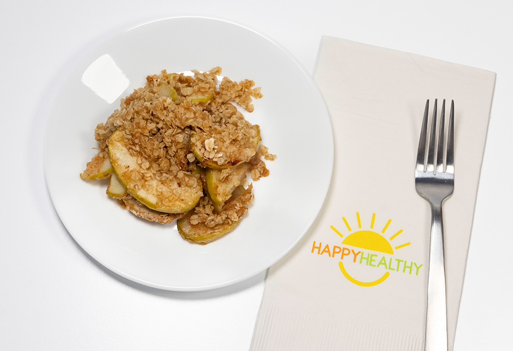 Apple crisp on a white plate next to a napkin and fork