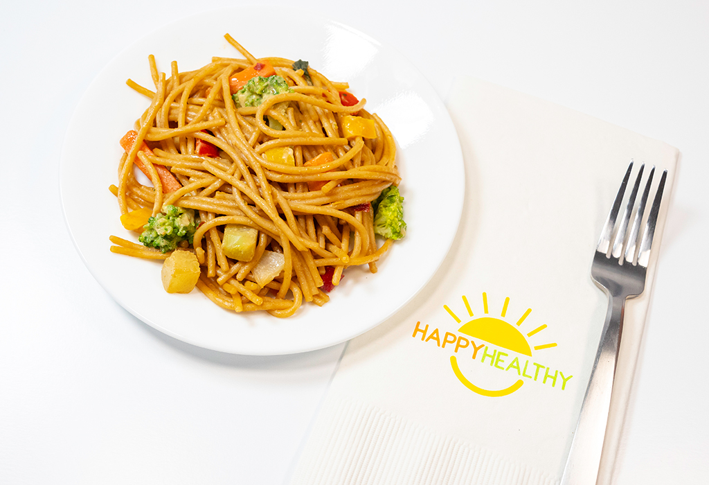 A white plate filled with Noodles and Peanut Sauce next to a fork and napkin