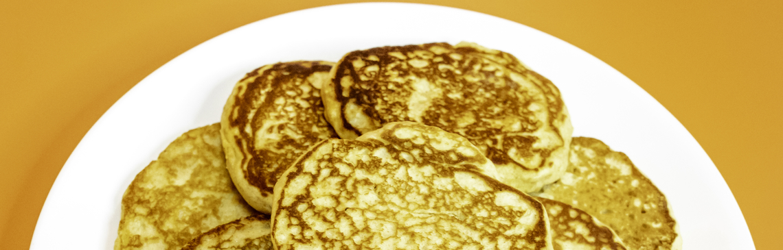 A white plate filled with pancakes on an orange background